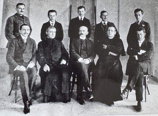 Pierwsze grono nauczycielskie Gimnazjum Realnego w roku szkolnym 1913/14. Siedzą od lewej: W. Kownacki, ks. E. Lurat, dyr. Cz. Odrowąż-Pieniążek, ks. W. Tomniczak, K. Brzozowski. Stoją od lewej: A. Małkowski, M. Peter, A. Pisz, W. Żarnecki, E. Sitowski